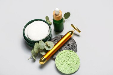 Facial massage tool with cosmetic dropper bottle, cotton pads, sponges and eucalyptus branches on light background
