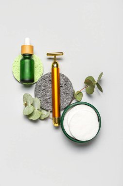 Facial massage tool with cosmetic dropper bottle, cotton pads, sponges and eucalyptus branches on light background