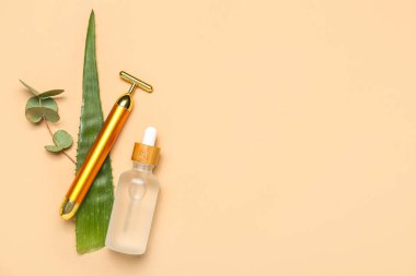 Facial massage tool with cosmetic dropper bottle, aloe vera leaf and eucalyptus on beige background
