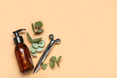 Facial massage tool with cosmetic bottle and eucalyptus branches on beige background