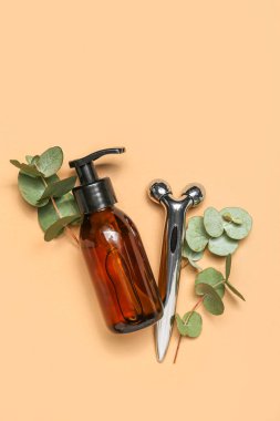 Facial massage tool with cosmetic bottle and eucalyptus branches on beige background
