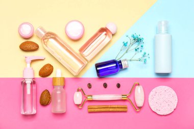 Facial massage tool with cosmetic products and natural components on color background