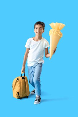 Little boy with yellow school cone and backpack on blue background