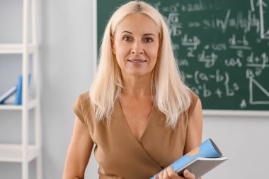 Mature Geography teacher with world map and book in classroom