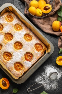 Baking tray with tasty apricot pie and sugar powder on dark background, closeup