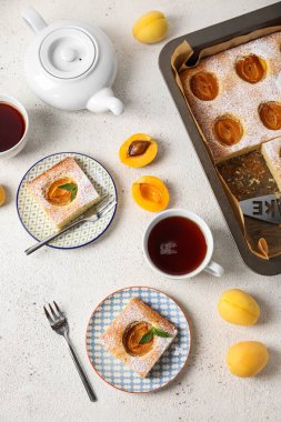 Composition with tasty apricot pie and cups of tea on light background