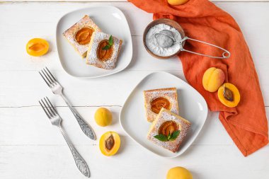 Plates with pieces of tasty apricot pie and sugar powder on light wooden background