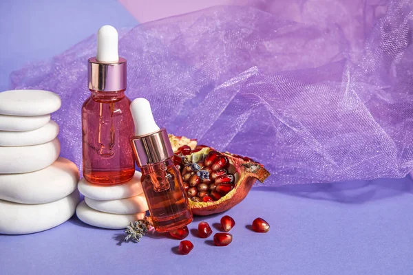 Composition with bottles of essential oil, pomegranate and spa stones on color background