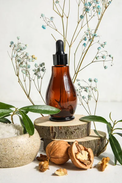 Composition with bottle of essential oil, walnuts and sea salt on light background