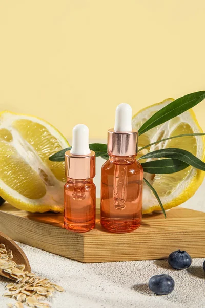 Wooden board with bottles of essential oil and lemons on table