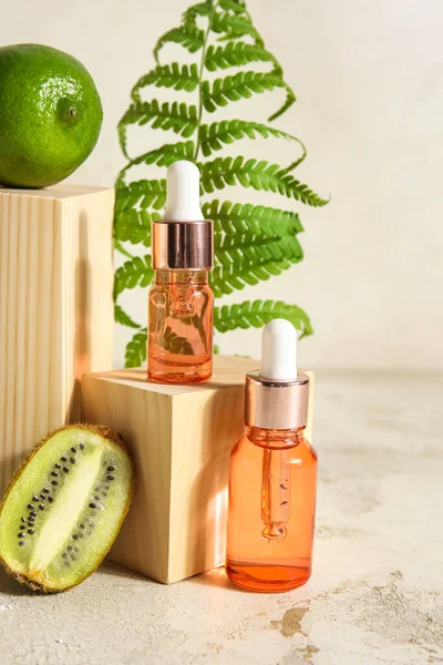 Composition with bottles of essential oil, fern leaf and wooden decor on light background
