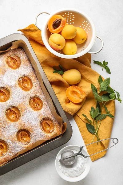 Composition with tasty apricot pie, fruits, sugar powder and mint on light background