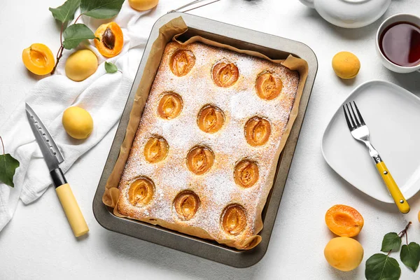 Baking tray with tasty apricot pie and fresh fruits on light background