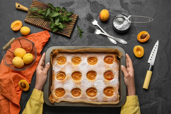 Female hands with tasty apricot pie, mint and sugar powder on dark background
