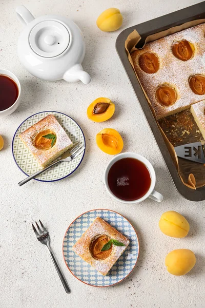Composition with tasty apricot pie and cups of tea on light background