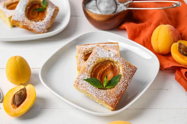 Plate with pieces of tasty apricot pie on light wooden background, closeup