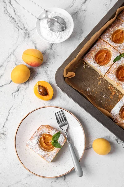 Plate with tasty apricot pie and sugar powder on light background
