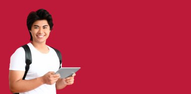 Happy young Asian man holding tablet computer on red background with space for text