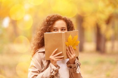 Sonbahar parkında kitabı olan genç bir Afro-Amerikalı kadın.