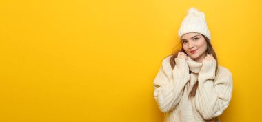 Pretty young woman in autumn sweater and hat on yellow background with space for text