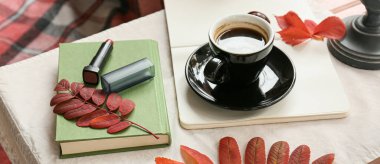 Cup of tasty coffee, autumn leaves, lipstick and notebooks on table 