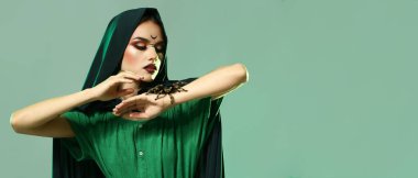 Young witch with spider on green background with space for text