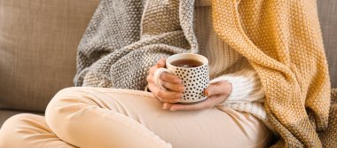Young woman drinking hot beverage while sitting on sofa at home, closeup