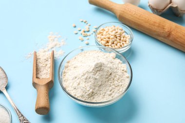 Bowl and scoop of flour on color background