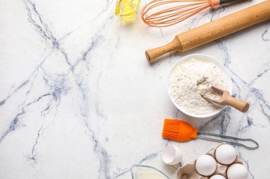 Bowl with flour, eggs and kitchen utensils on light background