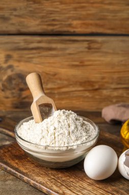 Bowl with flour and eggs on table against wooden background, closeup