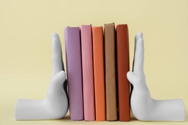 Books with stands in shape of hands on beige background
