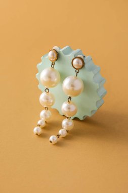 Showcase pedestal with elegant pearl earrings on beige background