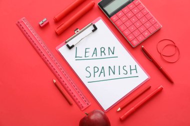 Clipboard with text LEARN SPANISH and stationery supplies on red background