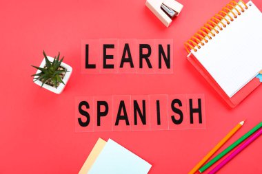 Text LEARN SPANISH with stationery and flowerpot on red background