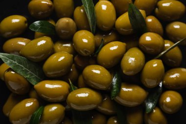 Delicious green olives and leaves as background, closeup