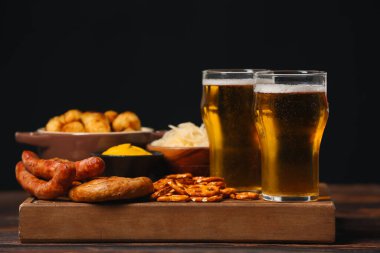 Board with glasses of beer and food on table against dark background. Oktoberfest celebration
