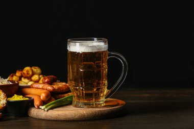 Board with mug of fresh beer and food on table against dark background. Oktoberfest celebration