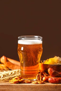 Board with mug of fresh beer and food on table against dark background. Oktoberfest celebration