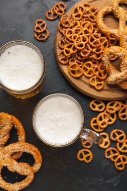 Mugs of fresh beer and pretzels on dark background. Oktoberfest celebration