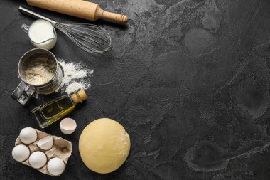Raw dough with ingredients and utensils on dark wooden background
