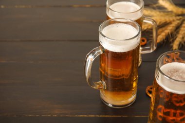 Mugs of fresh beer, pretzels and spikelets on wooden background, closeup. Oktoberfest celebration