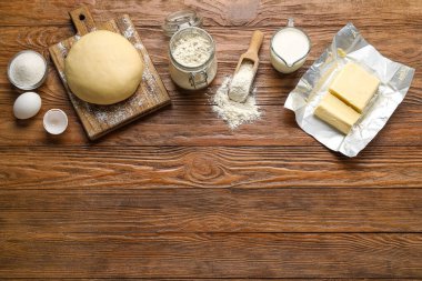 Raw dough with ingredients and utensils on wooden background