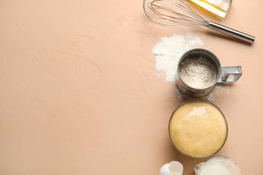 Bowl with raw dough, flour and whisk on color background