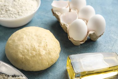 Raw dough, eggs and bottle of oil on color background, closeup