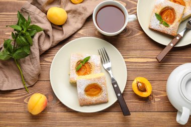 Plate with tasty apricot pie and cup of tea on wooden background