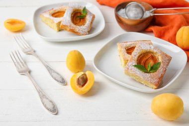 Plates with pieces of tasty apricot pie on light wooden background