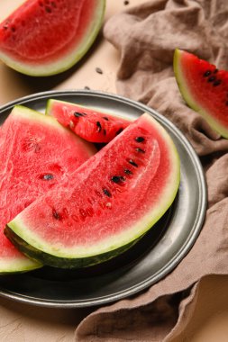 Plate with slices of watermelon and napkin on beige background, closeup