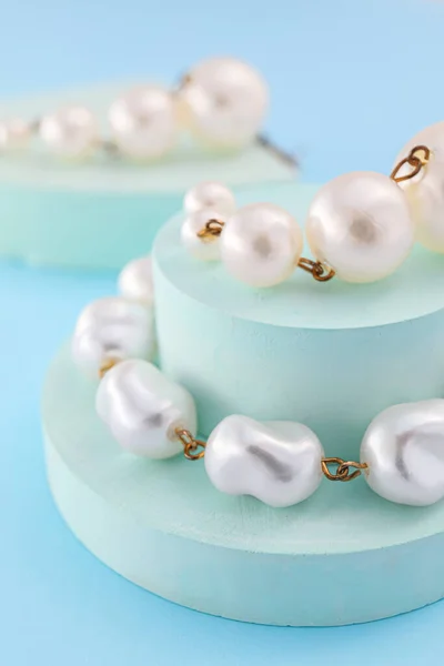 Showcase pedestals with pearl jewelry on blue background, closeup