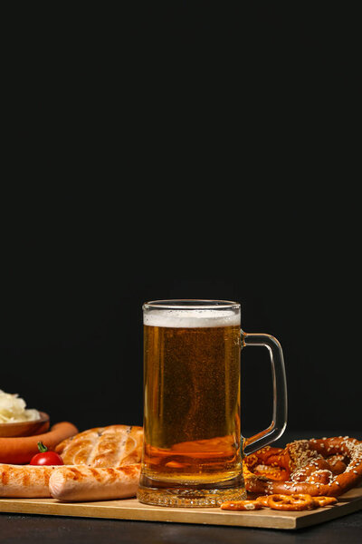 Board with mug of fresh beer and food on table against dark background. Oktoberfest celebration
