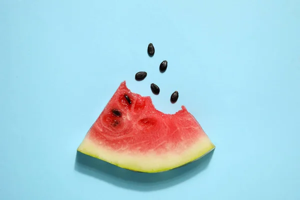 Slice of bitten watermelon with seeds on blue background